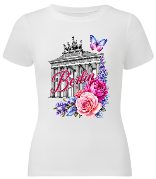 A white short-sleeve crewneck t-shirt featuring a colorful graphic print of the Brandenburg Gate with the word 'Berlin' in pink script, surrounded by pink and purple flowers and a butterfly.