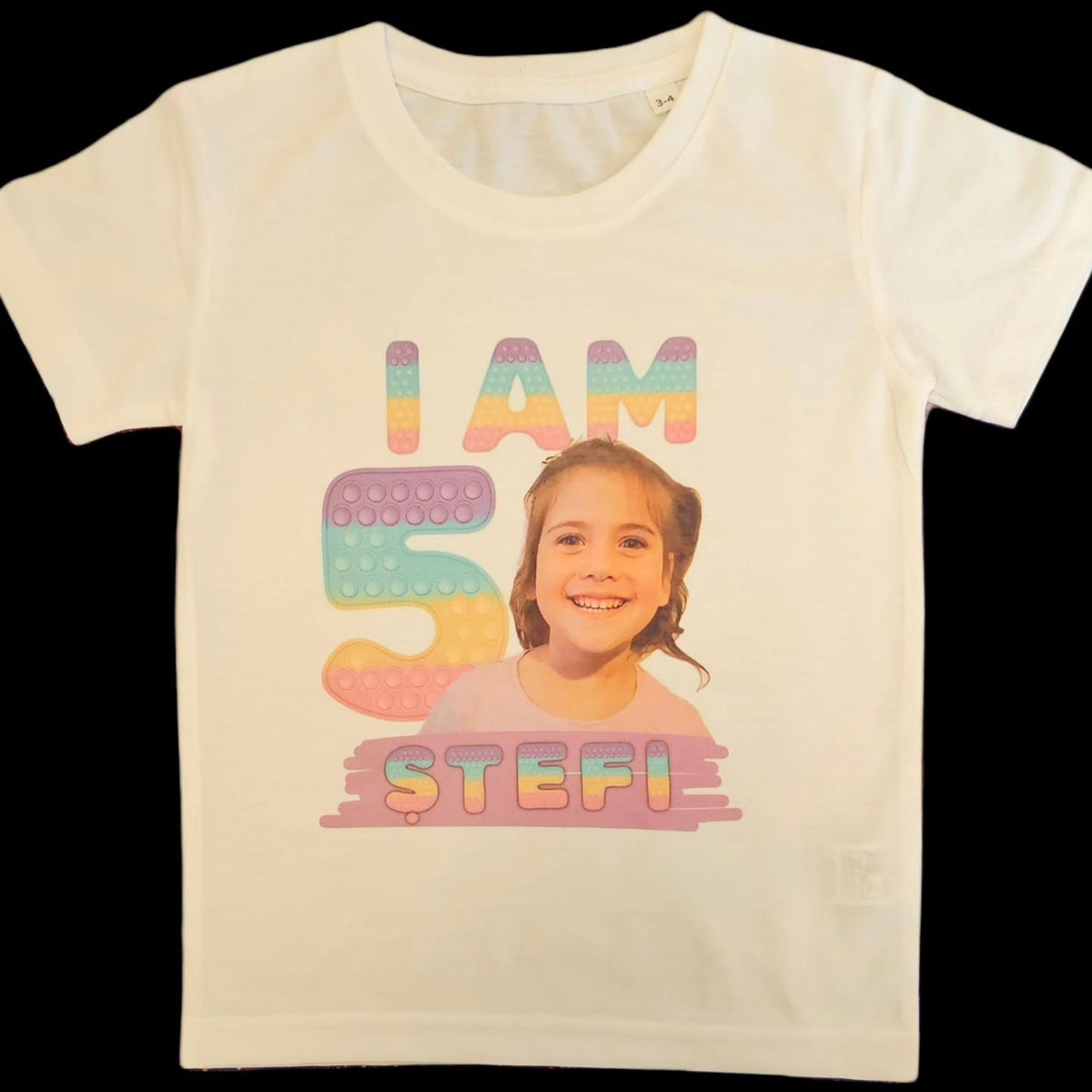 A white t-shirt with a colorful 'Pop It' design and text celebrating a I am, featuring the number 5 and the phrase and the name of the Birthday Girl.