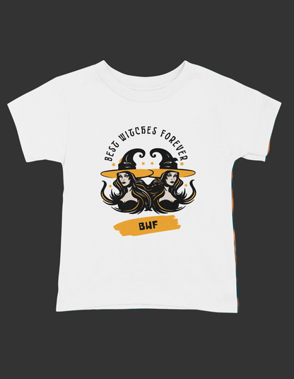 A white short sleeve t-shirt with a graphic print that reads 'Best Witches Forever' and includes images of two witch hats and a cauldron, surrounded by a fiery background.